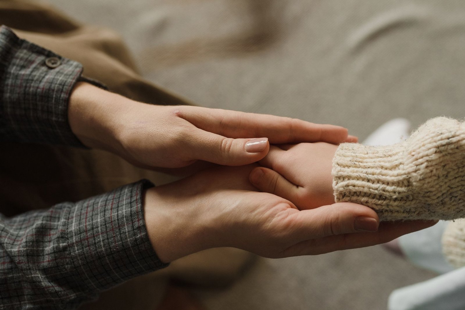 Mãos de adulto segurando as mãos de uma criança de blusa de tricô