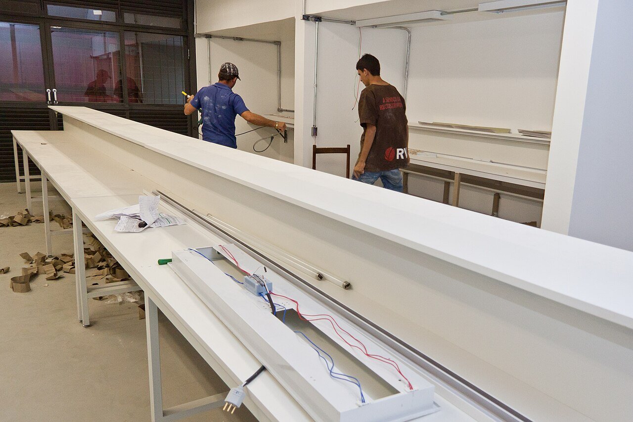Dois operários instalam a iluminação das bancadas de um laboratório da Universidade de Brasília
