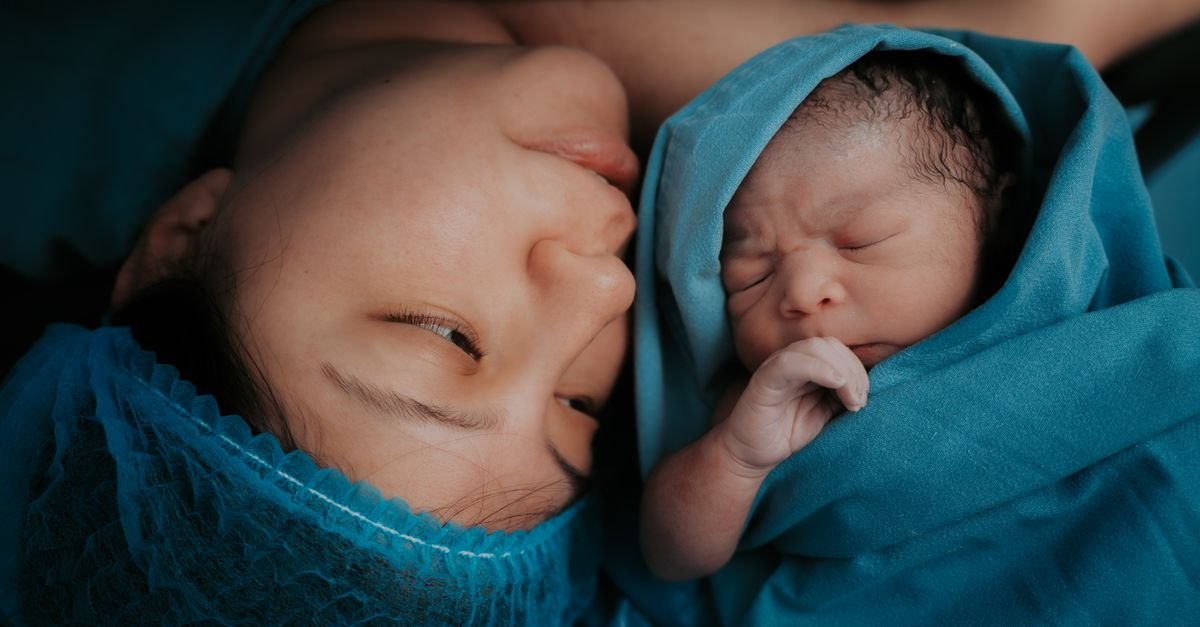 Mãe e recém-nascido lado a lado envoltos em tecido azul de ambiente hospitalar