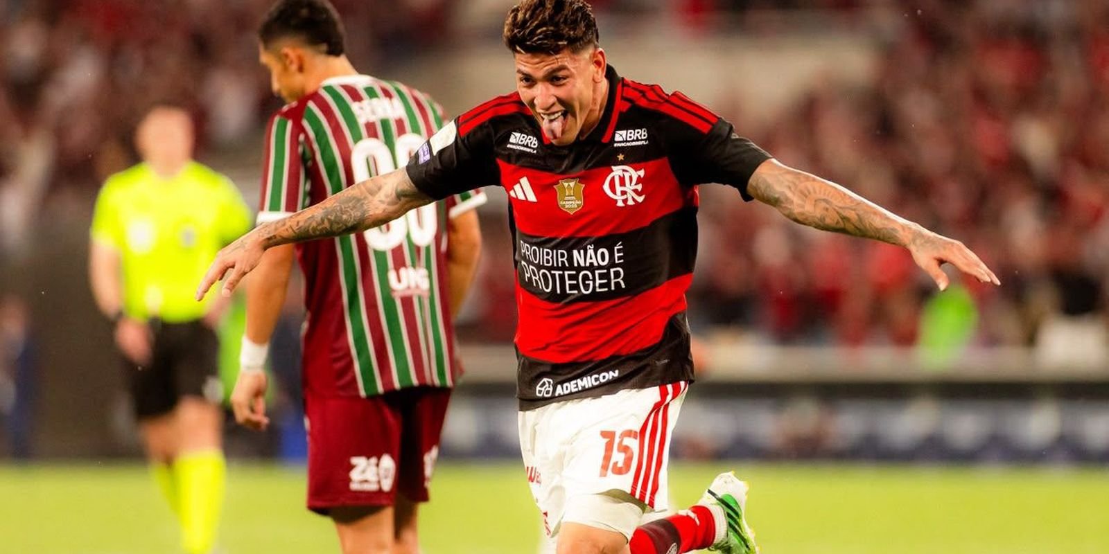 Jogador do Flamengo comemora gol com os braços abertos diante de um adversário do Fluminense