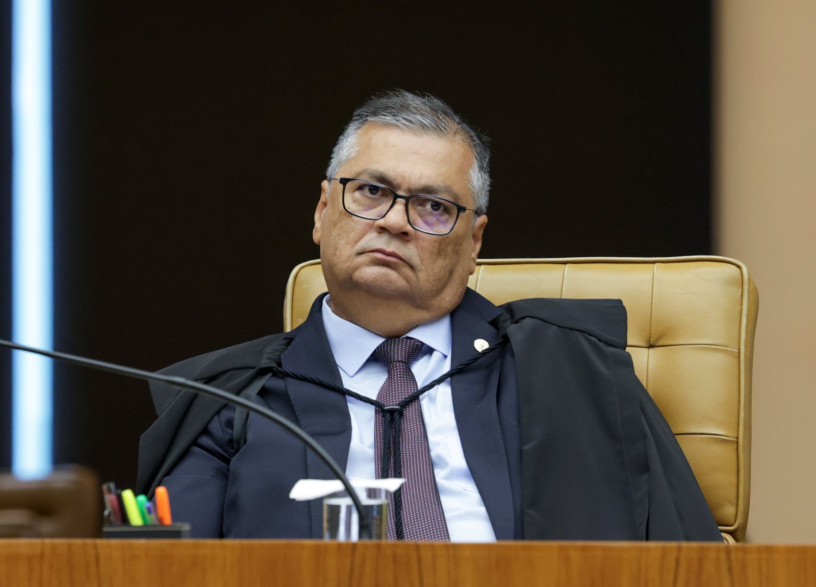 O ministro Flávio Dino, de toga e óculos, sentado na cadeira do plenário do STF durante sessão