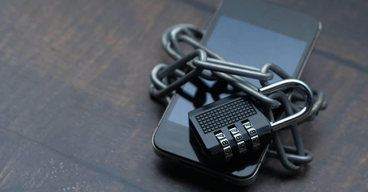 Celular envolto por corrente com cadeado de segredo sobre mesa de madeira