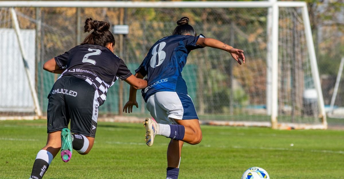 Duas jogadoras de futebol disputam a bola em campo gramado