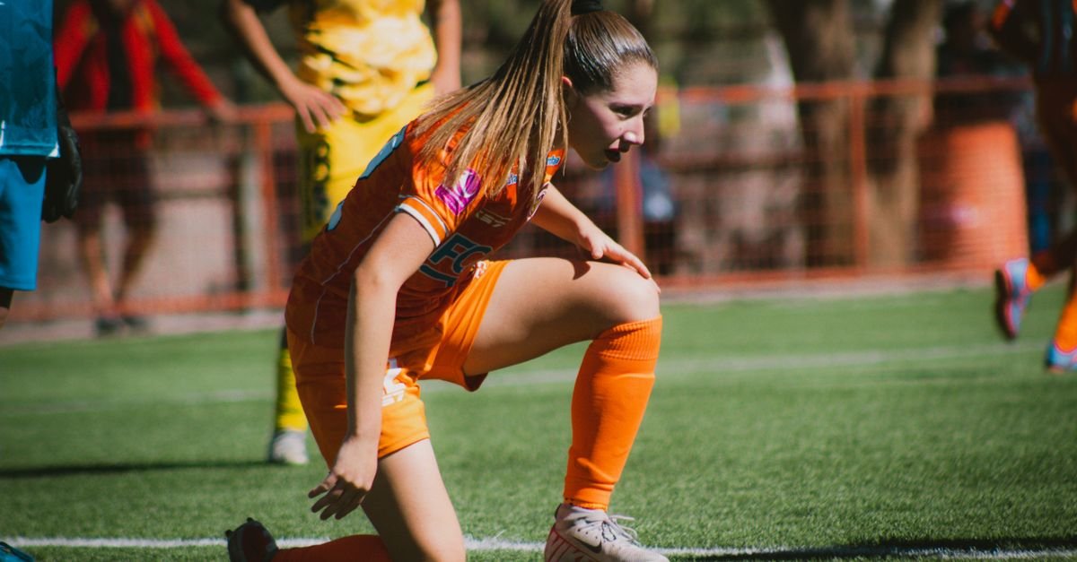 Jogadora de futebol feminino apoiada no joelho durante partida em campo gramado