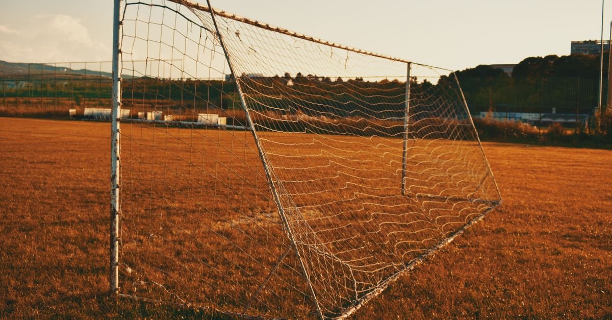 Trave e rede de gol de futebol em campo de grama ao entardecer
