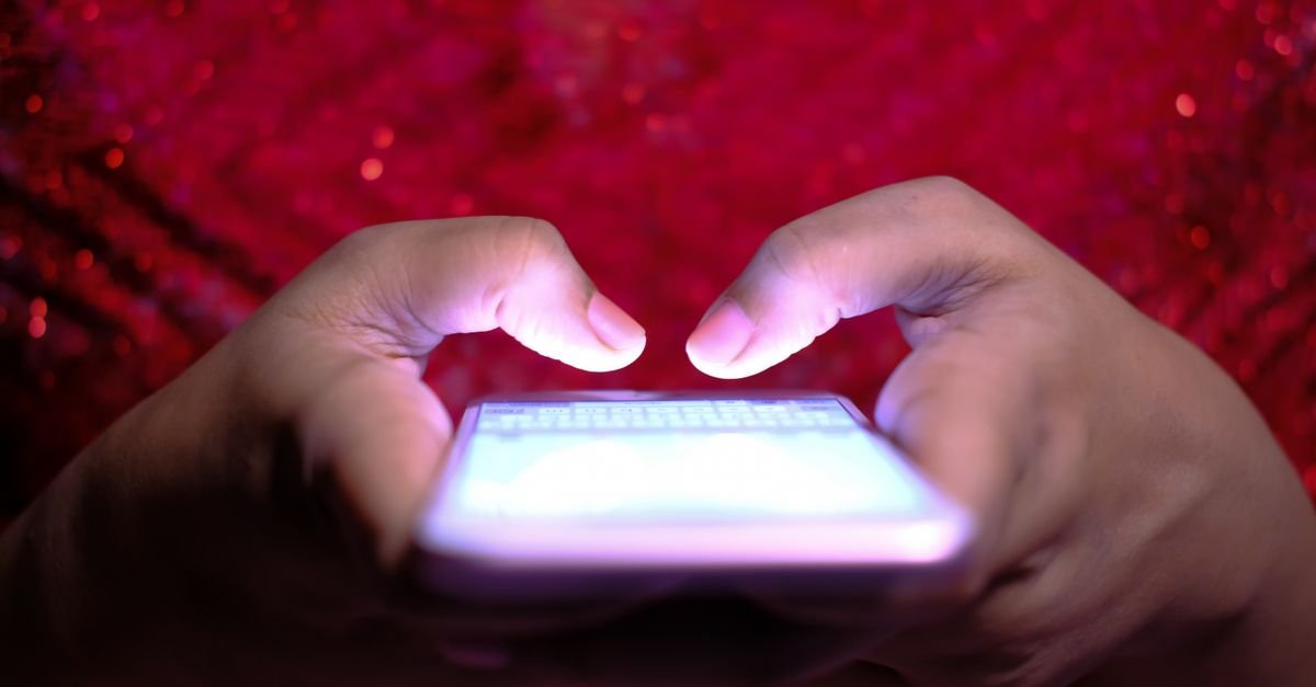 Mãos digitam em um celular com a tela acesa no escuro