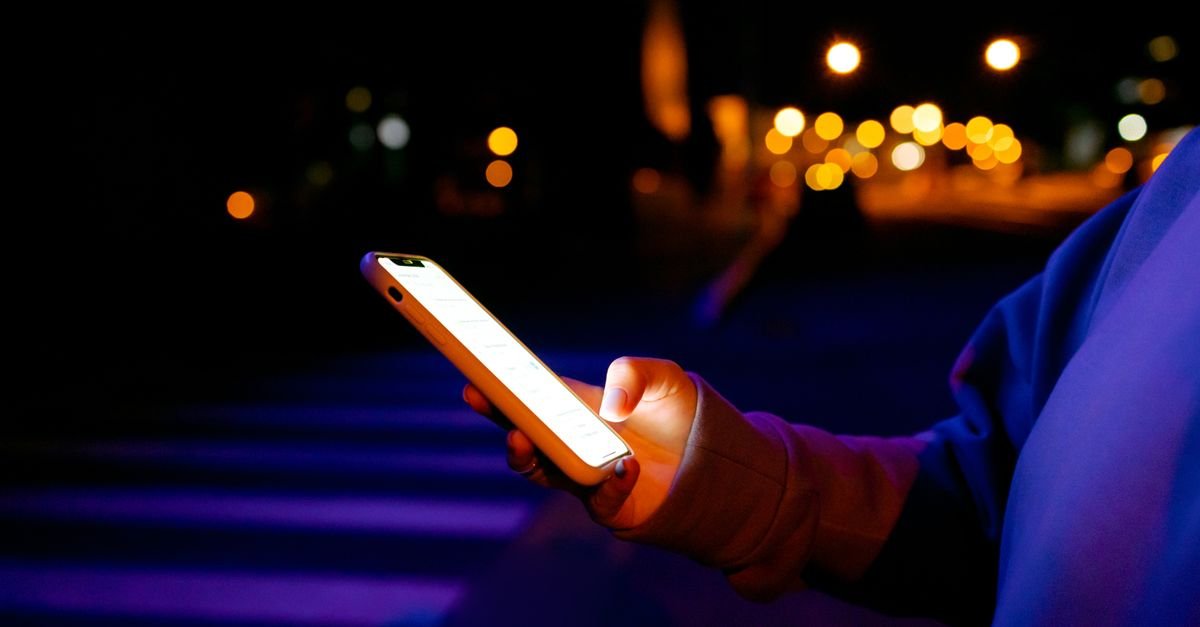 Mão segura celular com a tela acesa durante a noite, em imagem ilustrativa de golpe aplicado por mensagem