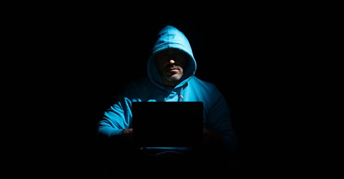Pessoa de capuz usa notebook em ambiente escuro, em imagem que ilustra fraude financeira on-line