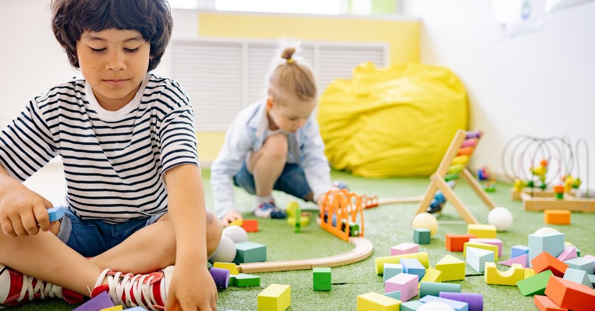 Crianças brincam com blocos de montar e trilhos em sala de educação infantil, imagem ilustrativa