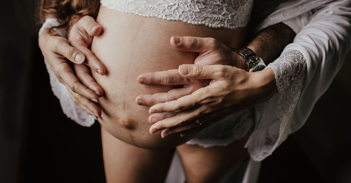 Mãos de um casal apoiadas sobre a barriga de uma mulher grávida