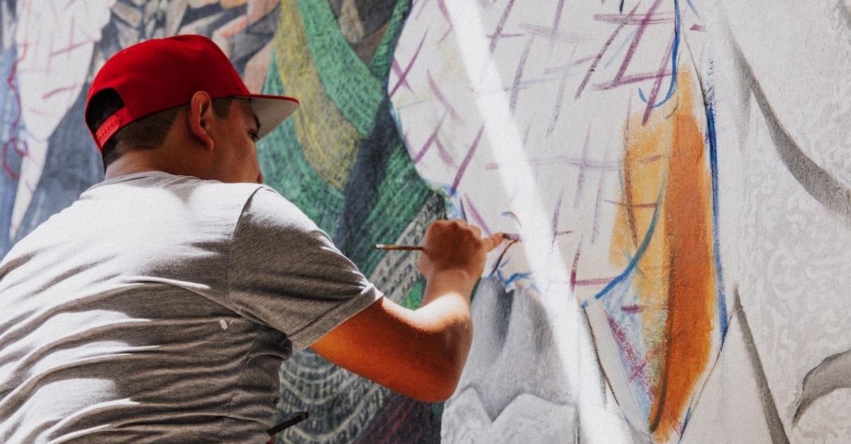 Artista de bone vermelho pinta mural colorido em muro urbano durante o dia