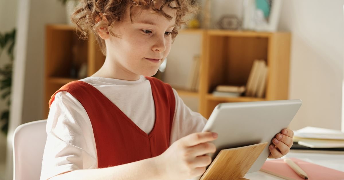 Criança usa tablet para estudar sobre uma mesa com caderno e lápis