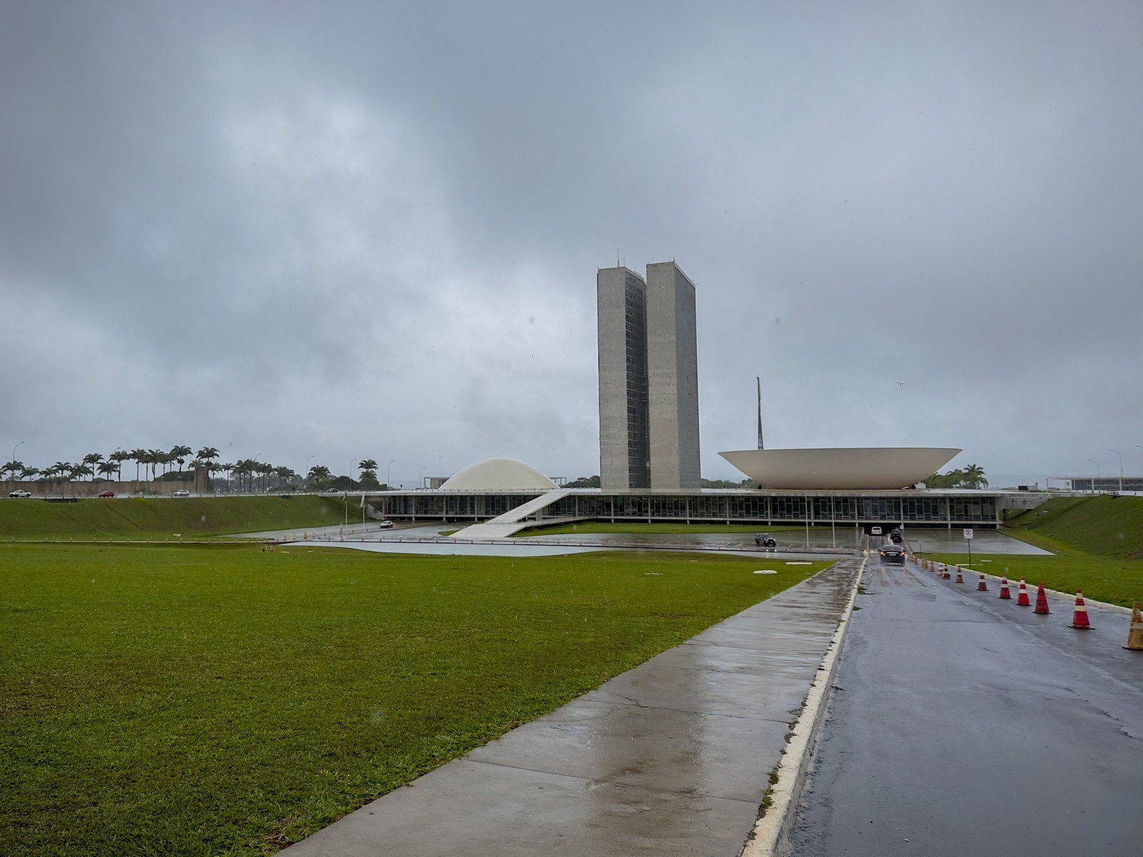 Palácio do Congresso Nacional sob céu carregado, com o gramado e a pista molhados pela chuva