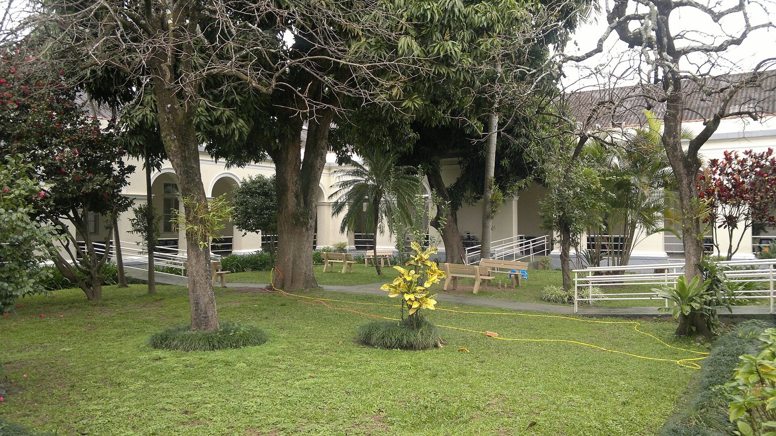 Pátio arborizado com bancos e rampas de acessibilidade em instituição de longa permanência para idosos
