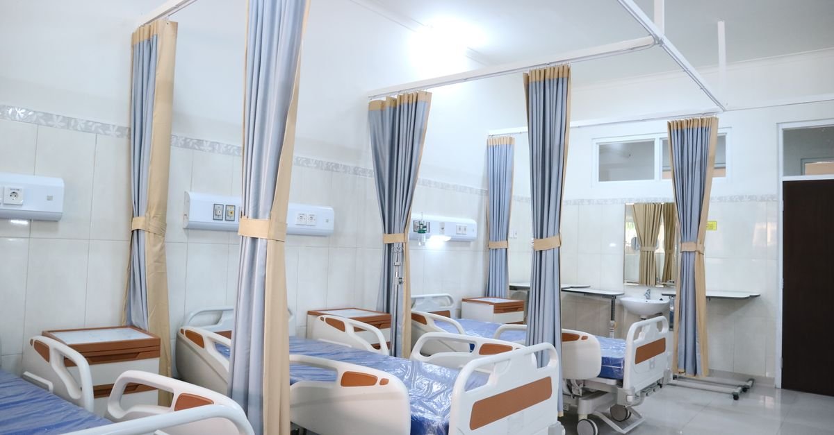 Enfermaria hospitalar com leitos vazios separados por cortinas