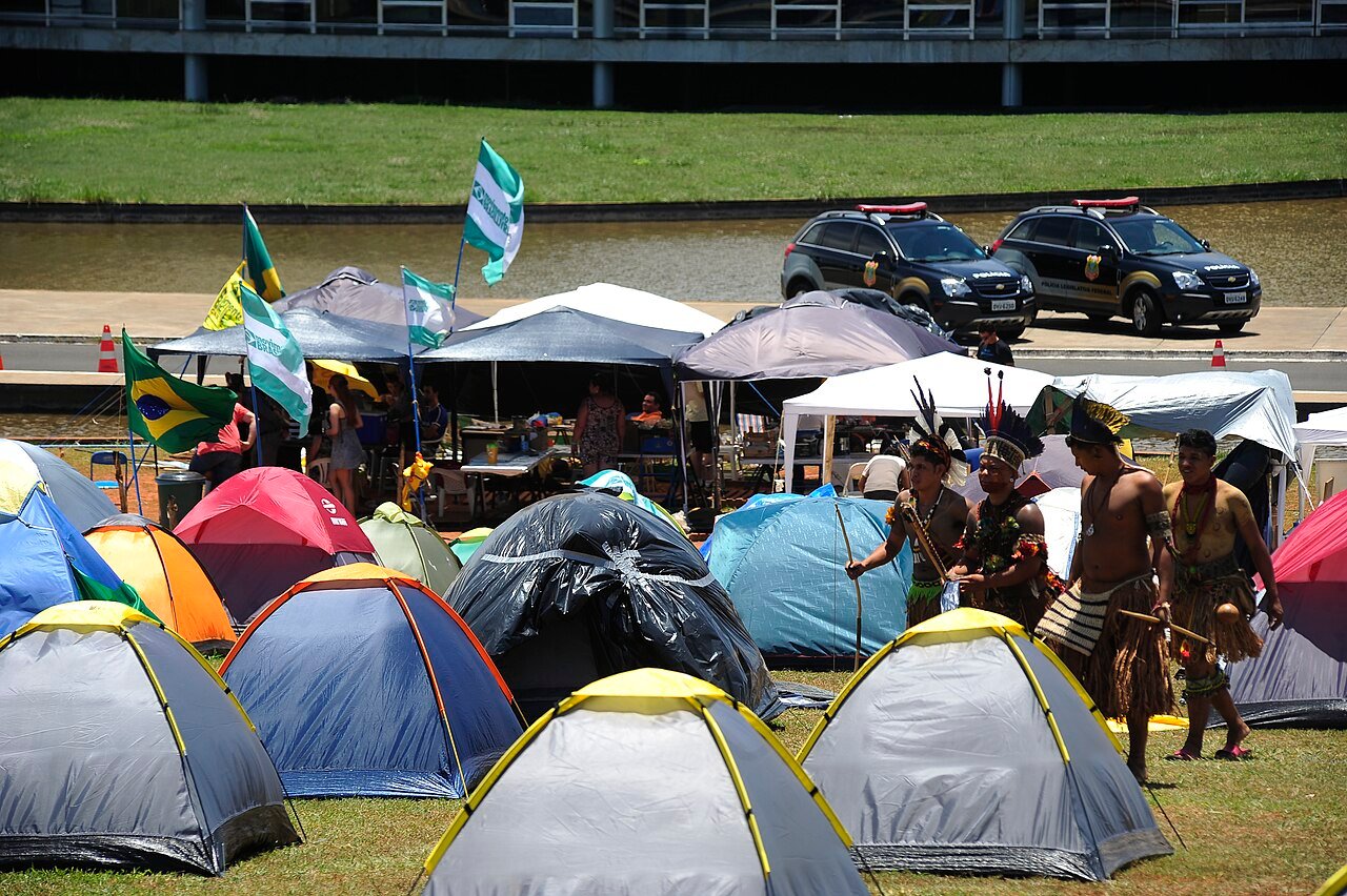 Indígenas em trajes tradicionais caminham entre barracas de acampamento na Esplanada dos Ministérios