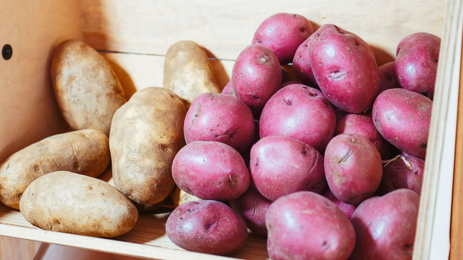 Batatas marrons e roxas em uma caixa de madeira, em close