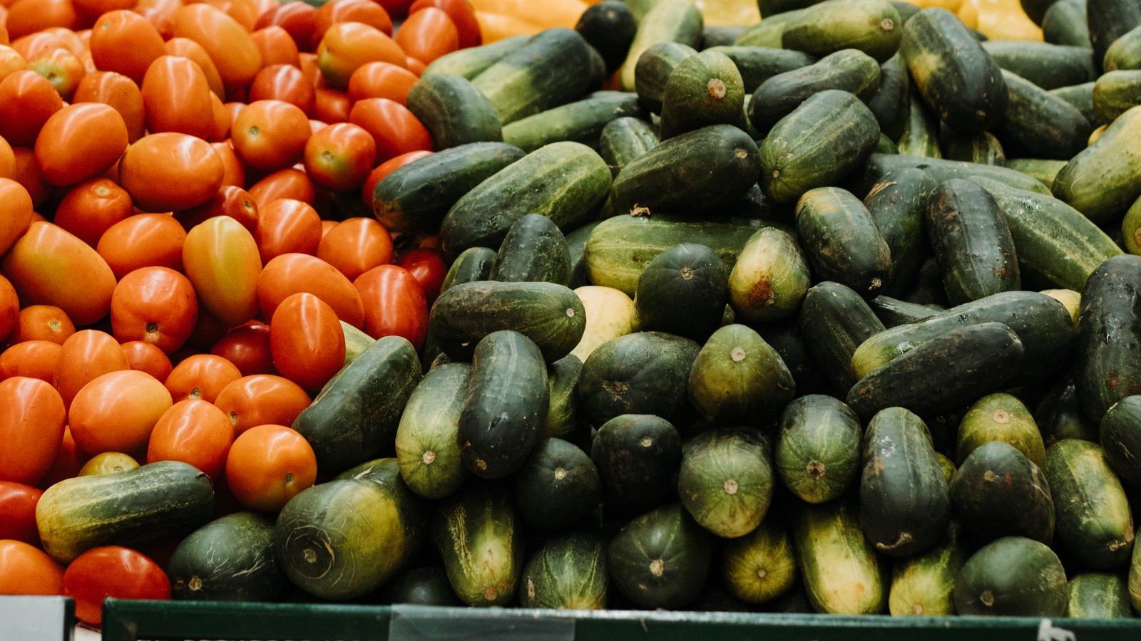 Tomates e pepinos empilhados em banca de hortifrúti de supermercado brasileiro