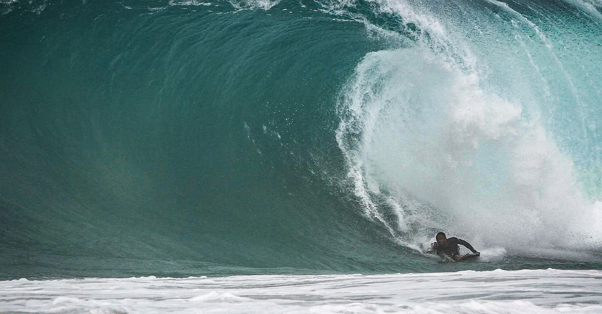 Surfista dentro do tubo de uma onda grande e escura, com espuma branca ao redor