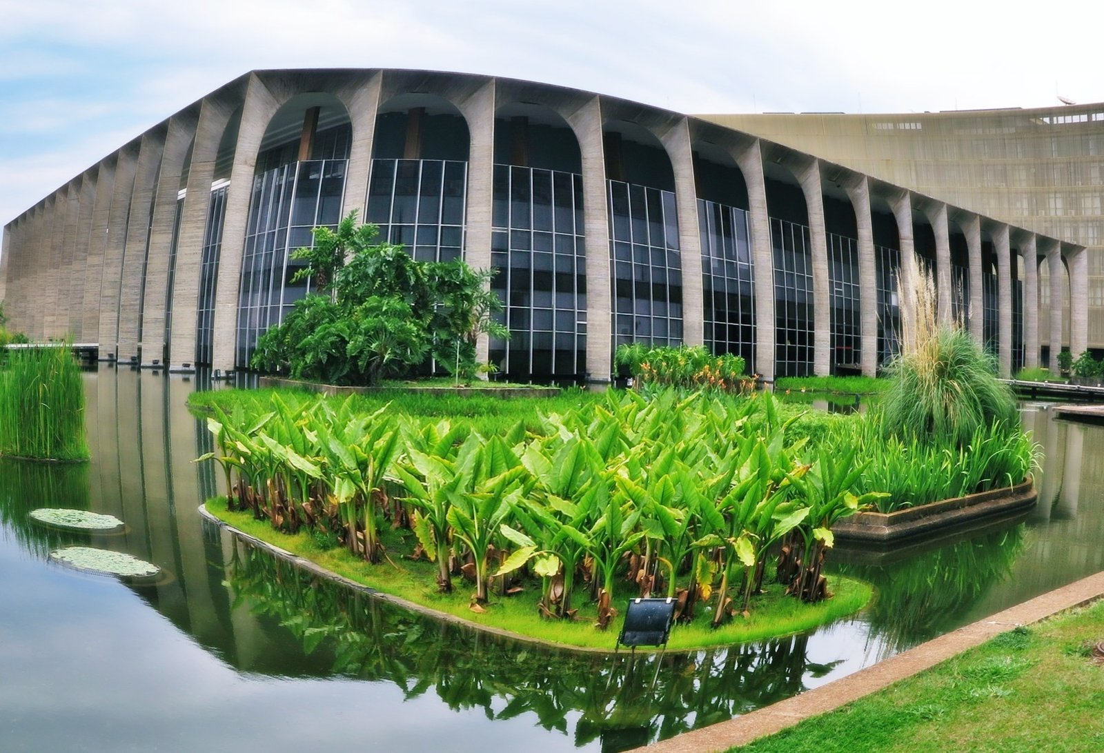 Fachada de arcos do Palácio do Itamaraty, em Brasília, refletida no espelho d'água com vegetação aquática