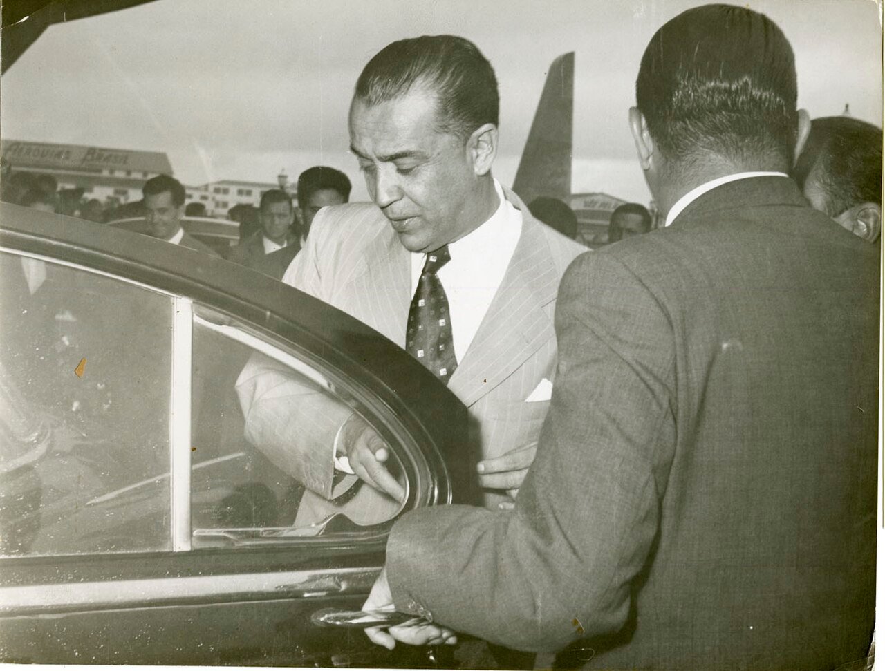 Juscelino Kubitschek entra em um carro cercado de pessoas em foto histórica em preto e branco