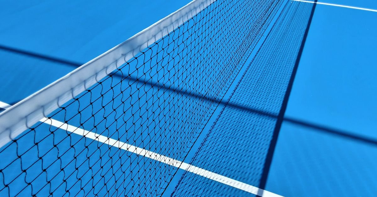 Rede e linhas brancas de uma quadra de tenis de piso duro azul vista de angulo baixo