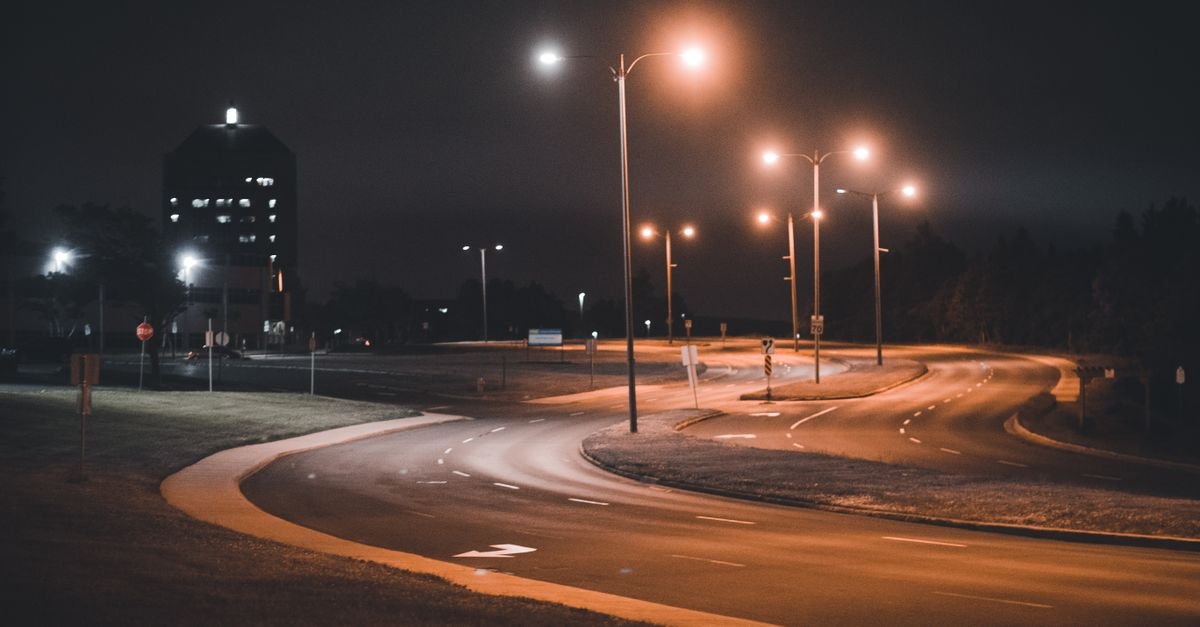 Via urbana vazia iluminada por postes de luz durante a madrugada