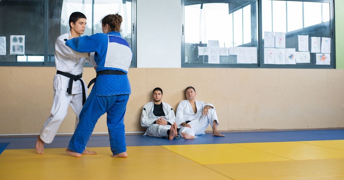 Judocas de quimono branco e azul treinam em tatame de dojo