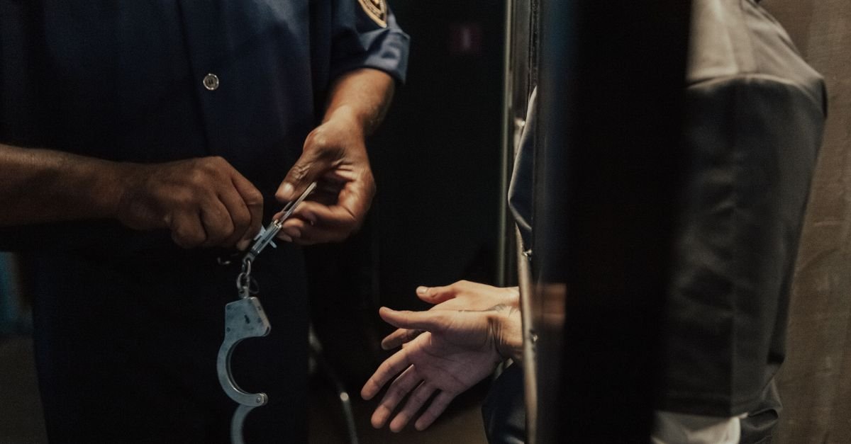 Agente de segurança com algemas diante de mãos estendidas entre grades
