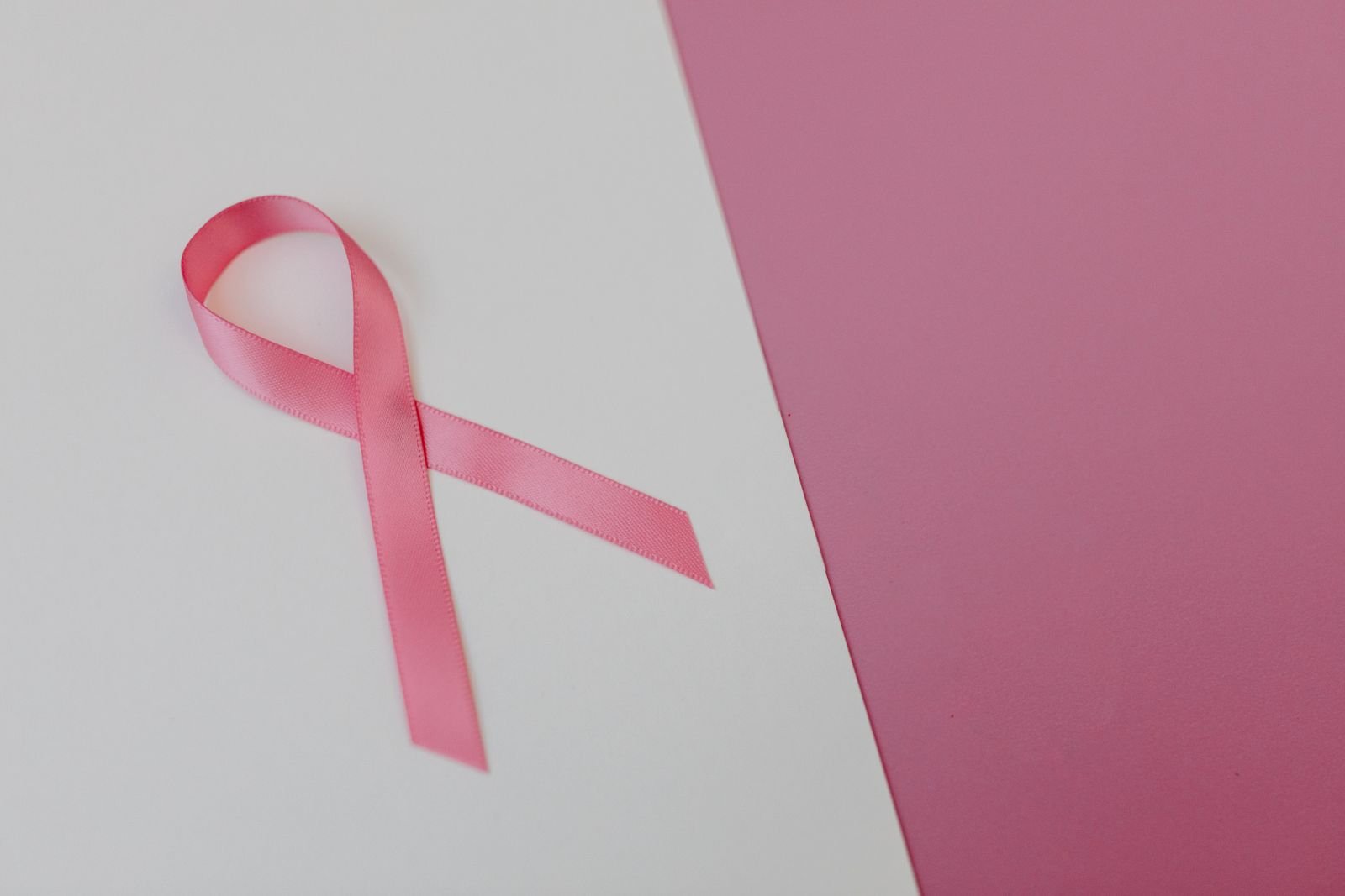 Laço de fita rosa sobre superfície clara com fundo rosa, símbolo do Outubro Rosa