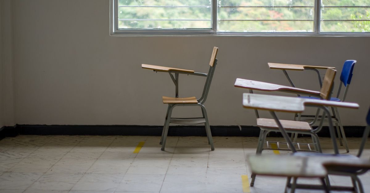 Sala de aula vazia com carteiras escolares de madeira diante de uma janela