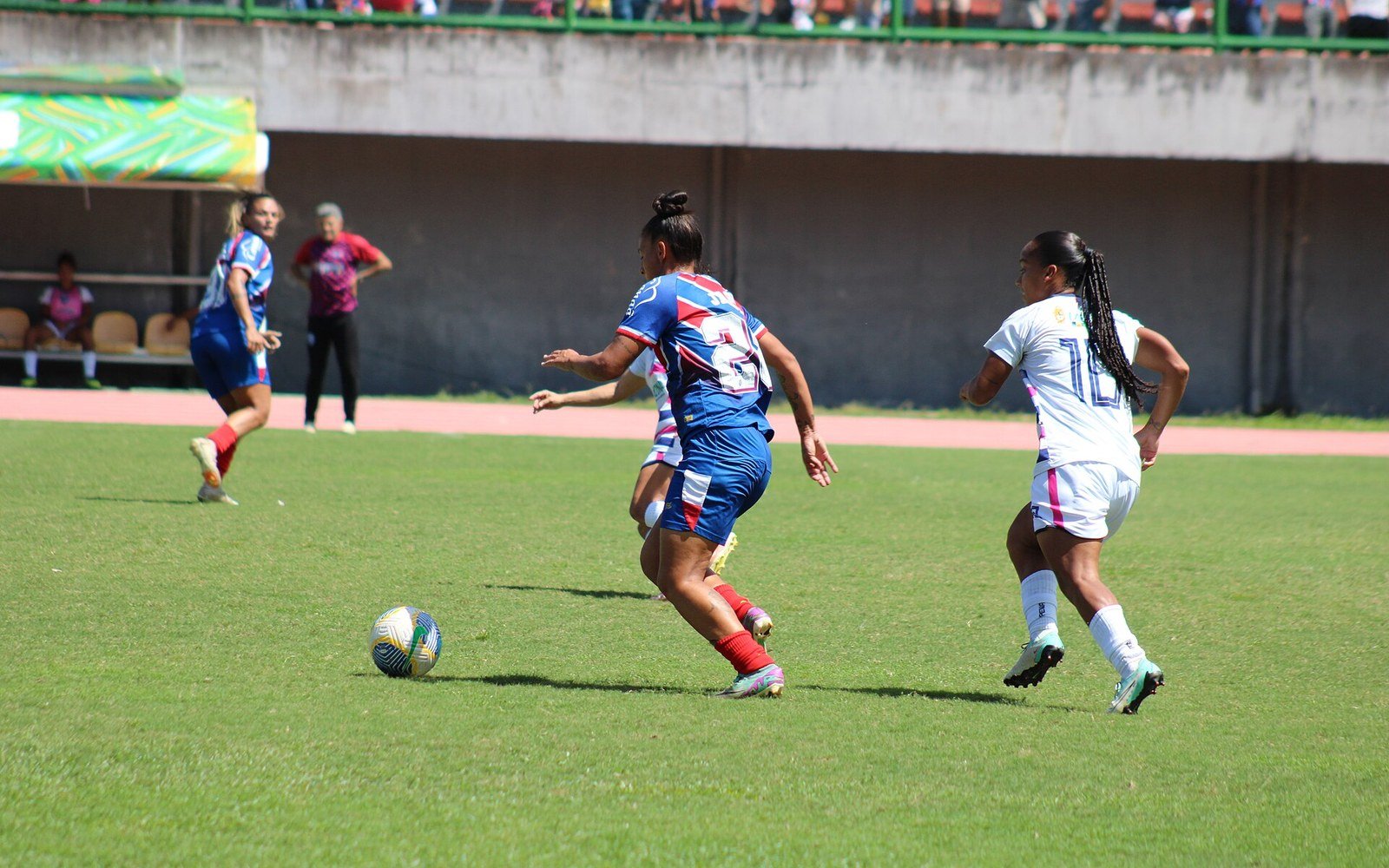 Jogadoras de futebol feminino disputam a bola em gramado, durante partida oficial no Brasil