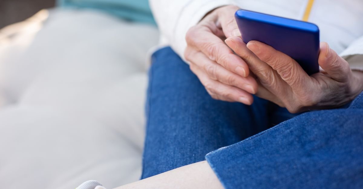 Mãos de uma pessoa idosa segurando um telefone celular