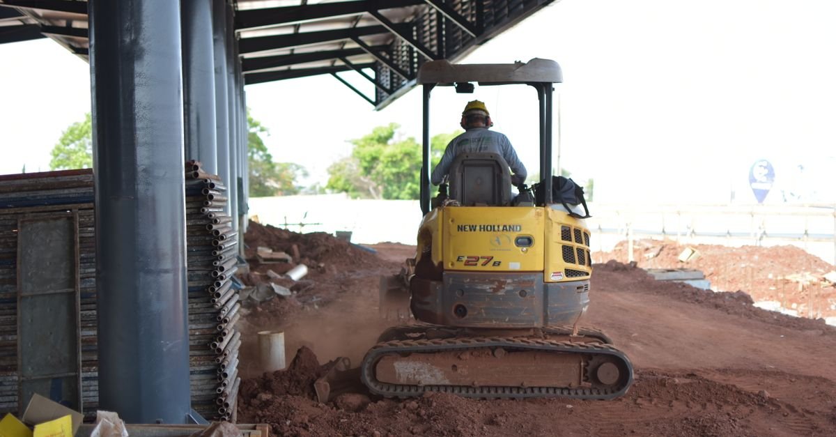 Máquina escavadeira movimentando terra vermelha em canteiro de obras