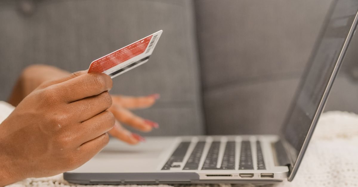 Pessoa segura um cartão em uma das mãos enquanto usa um notebook para fazer uma compra online