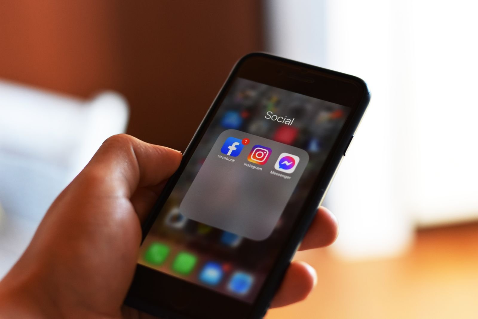 Mão segura celular com os ícones de Facebook, Instagram e Messenger numa pasta de aplicativos