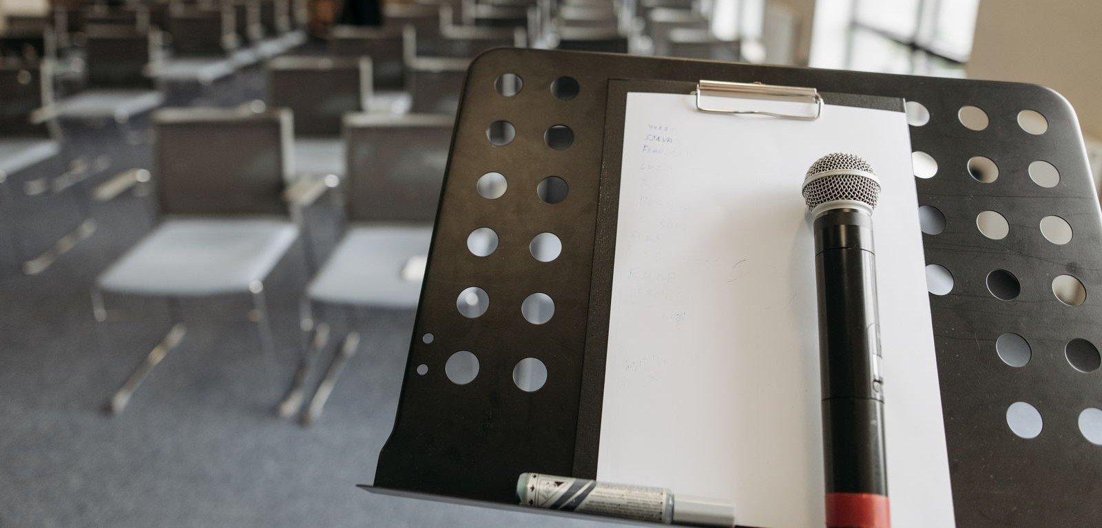 Microfone sobre estante de partitura em sala de treinamento com cadeiras em fileiras, imagem ilustrativa