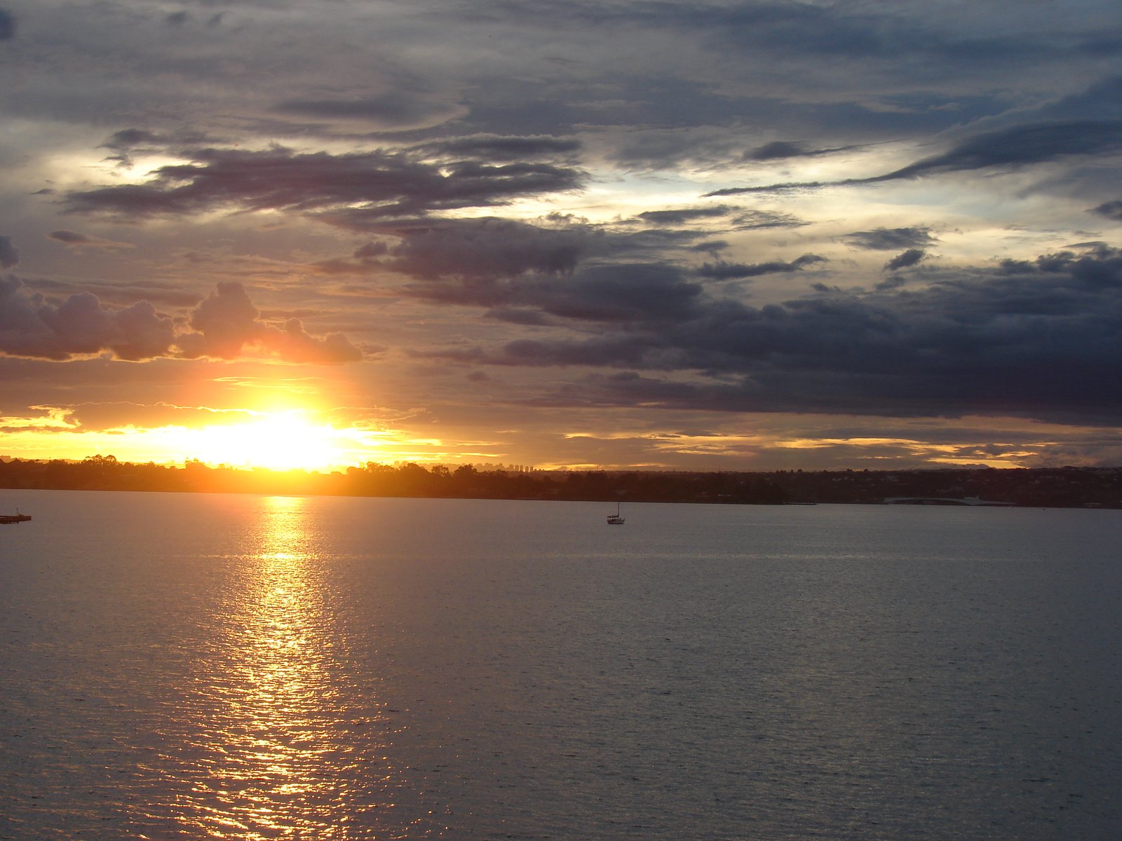 Lâmina d'água do Lago Paranoá ao fim da tarde, com veleiro ancorado e a orla de Brasília ao fundo