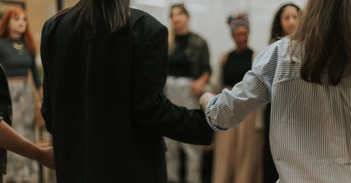 Roda de mulheres de mãos dadas durante encontro em ambiente fechado
