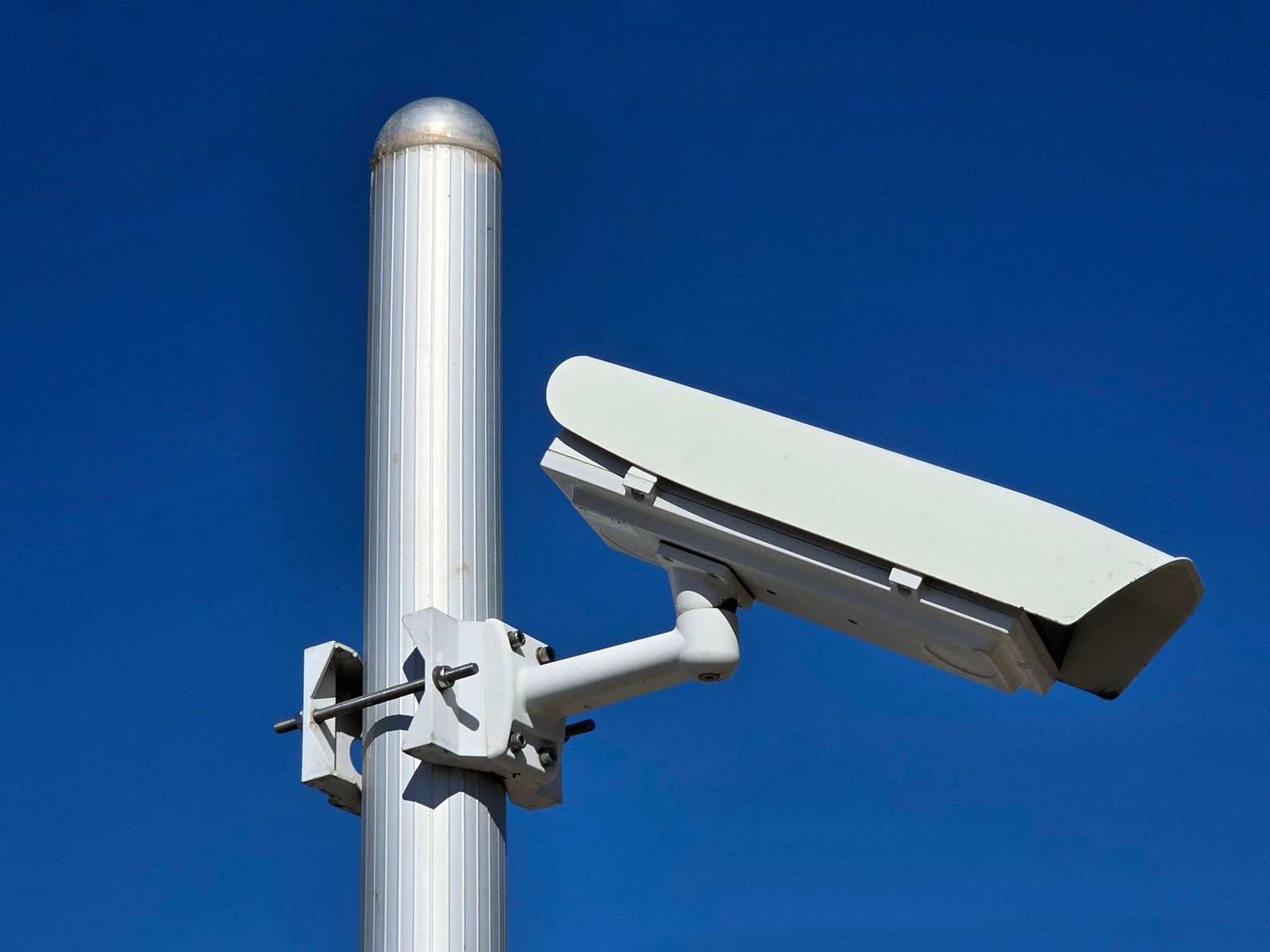 Câmera de videomonitoramento branca instalada em poste, com o céu azul ao fundo