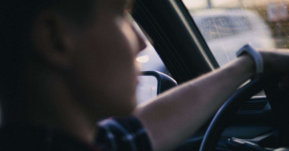 Motorista visto de trás, desfocado, com a mão sobre o volante durante a condução