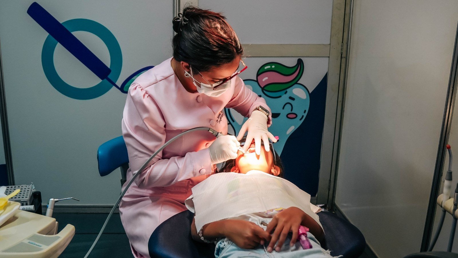 Dentista de jaleco rosa atende menina na unidade do Odonto em Ação em Cidade Ocidental