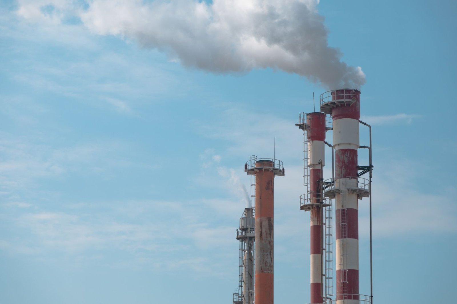Três chaminés industriais listradas de vermelho e branco soltam fumaça contra o céu azul (foto ilustrativa)