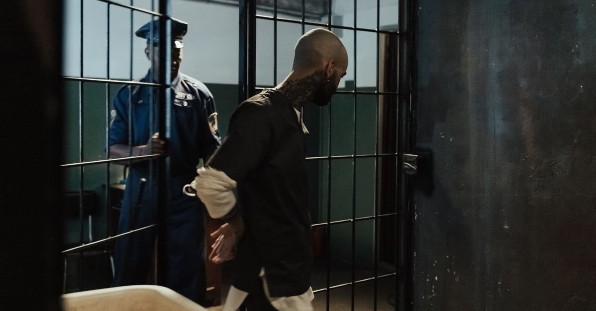 Agente conduz preso algemado por corredor de cela