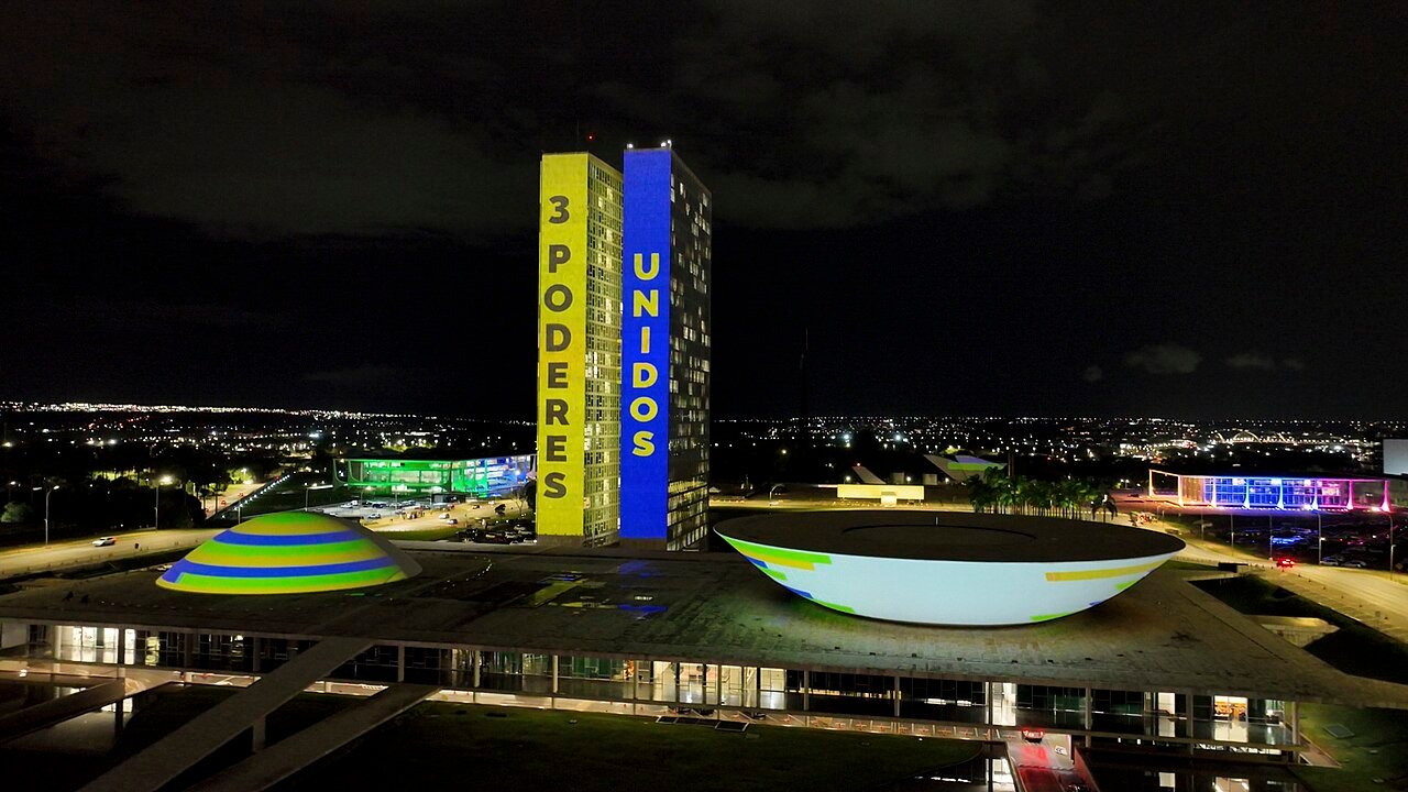 Congresso Nacional iluminado à noite com a projeção 3 Poderes Unidos, do Pacto Nacional de Enfrentamento ao Feminicídio