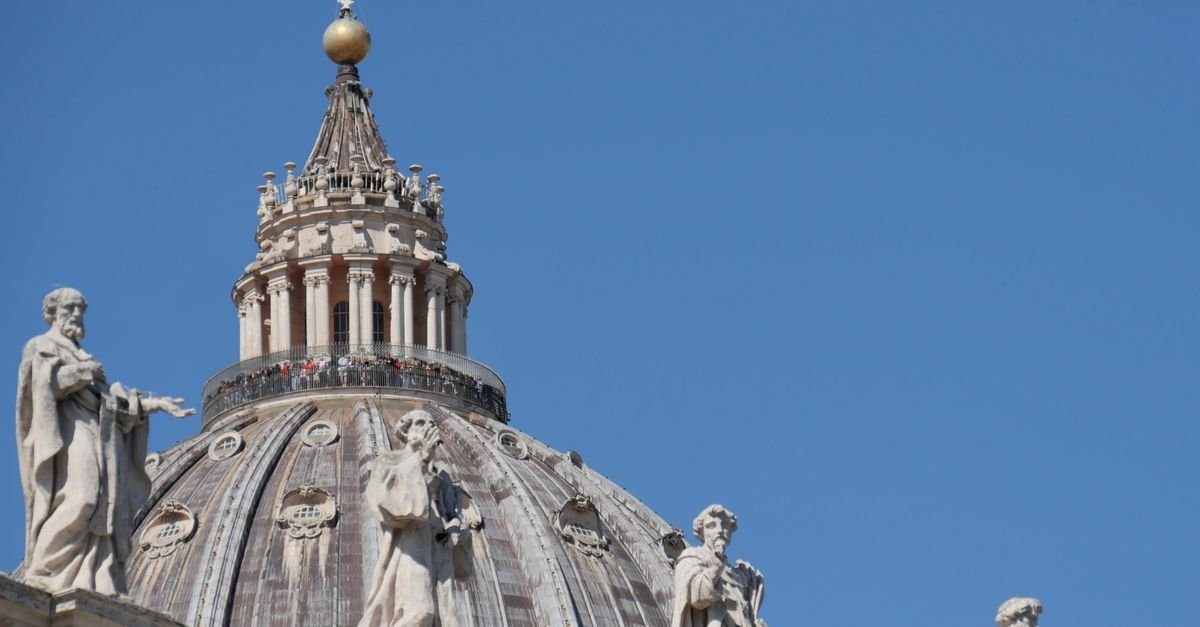 Cúpula da Basílica de São Pedro, no Vaticano, sob céu azul, com estátuas em primeiro plano