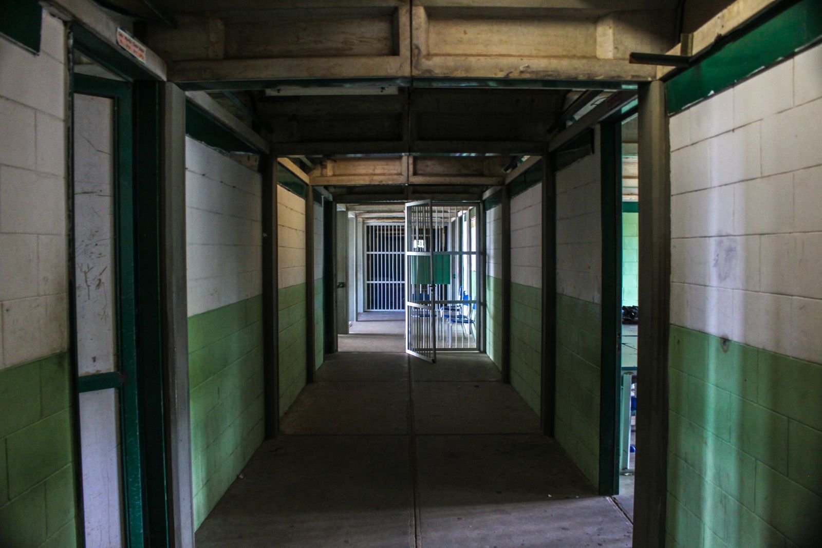 Corredor de uma unidade prisional com paredes de azulejo branco e verde e uma grade aberta ao fundo