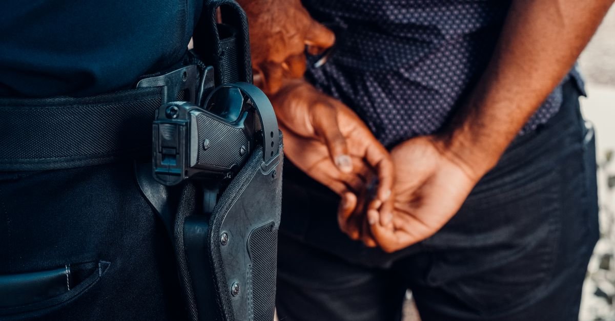 Policial de uniforme ao lado de homem com as mãos para trás, em detalhe de abordagem; foto ilustrativa de arquivo