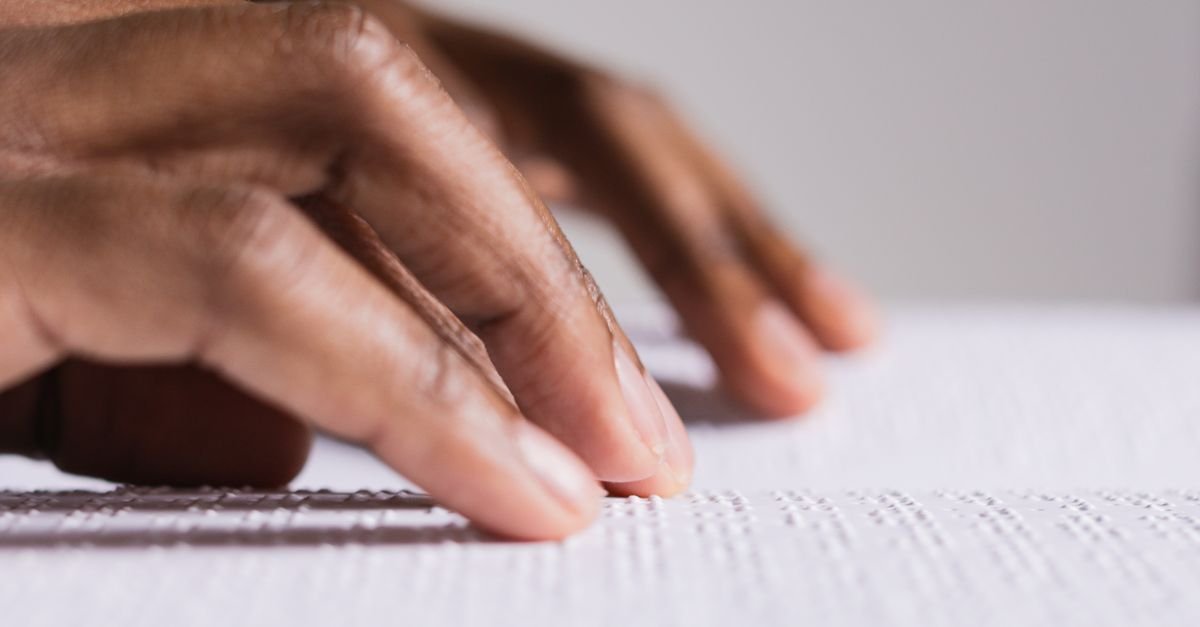 Mãos percorrendo texto em braille impresso em relevo sobre uma folha branca