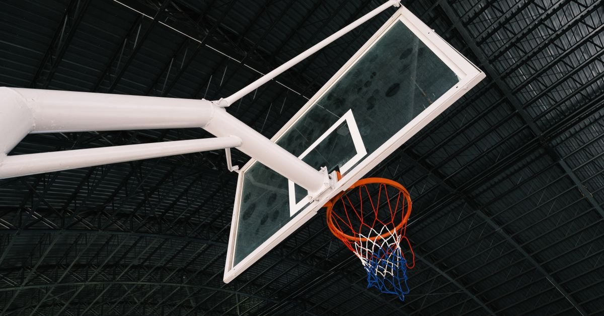 Tabela e aro de basquete vistos de baixo dentro de um ginasio coberto
